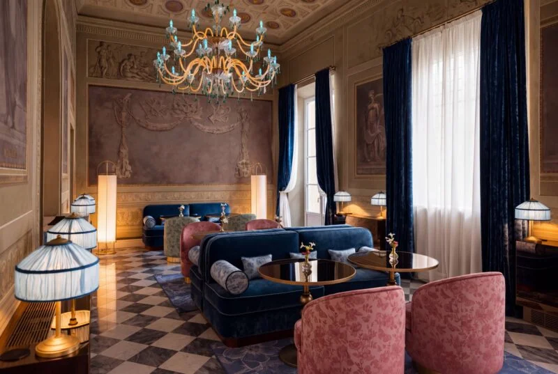 Palazzo Sogni 休息厅，蓝色天鹅绒沙发、粉色扶手椅与棋盘格地面