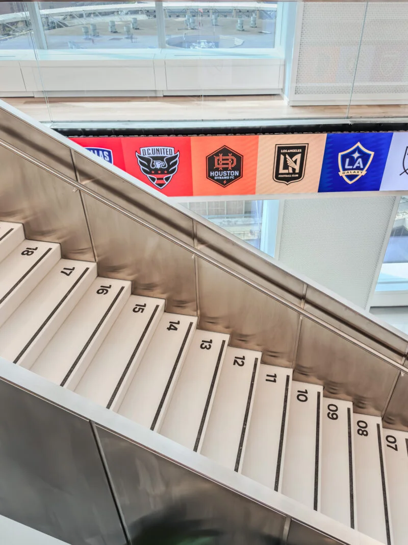 楼梯台阶标有 7 至 18 的数字，上方是 MLS 总部各球队标志横幅