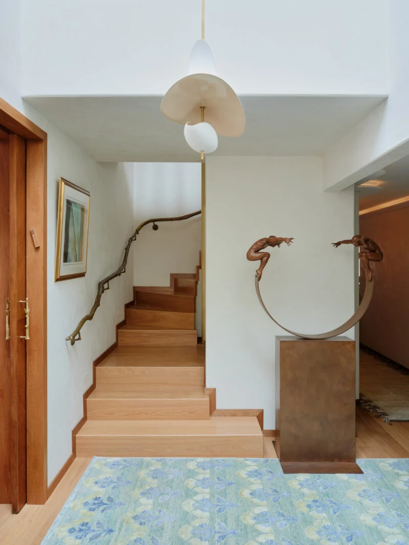 木质楼梯配有树枝状扶手，前景是立在弧形金属底座上的双人雕塑。